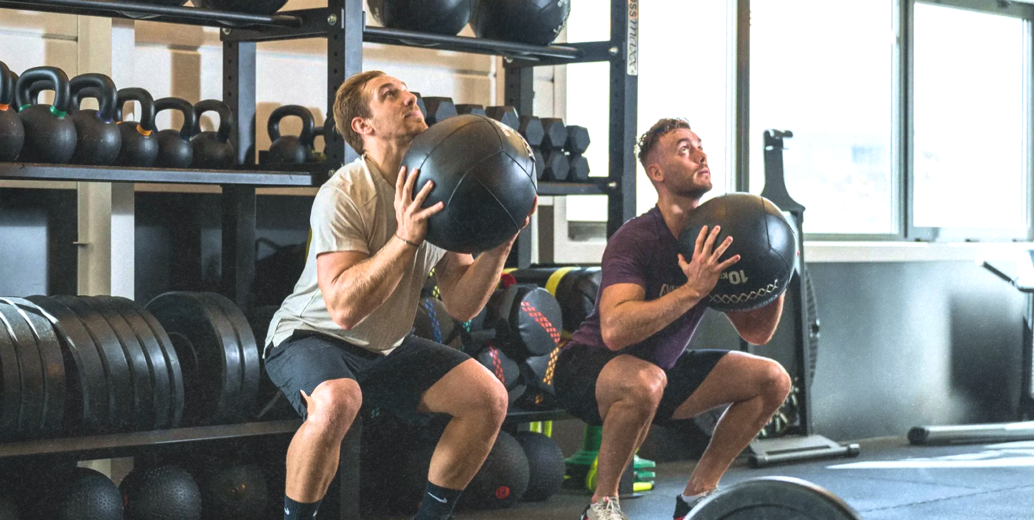 Deux collaborateurs en squat avec ballon lesté dans une salle de sport d'entreprise